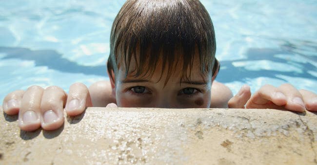 Boy peaking over the edge of a swimming pool