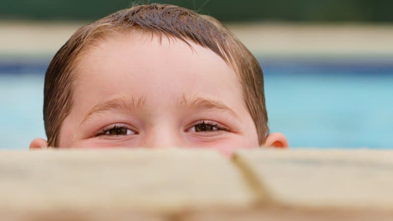 Closeup of a boy peeking over the edge of a pool, with pool coping in the foreground