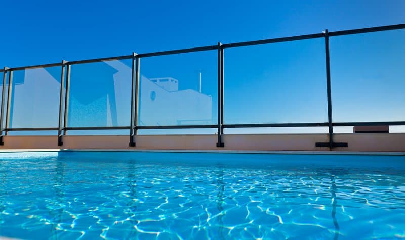 View of an inground swimming pool with a stylish glass pool fence
