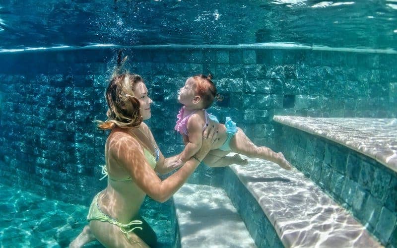Underwater view of a smiling mother holding her baby near the swimming pool steps