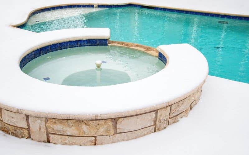 Picture of an inground swimming pool and spa during winter, with snow all around