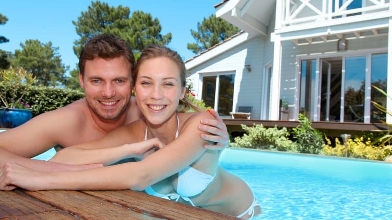 Closeup of a young couple smiling while soaking in an inground swimming pool