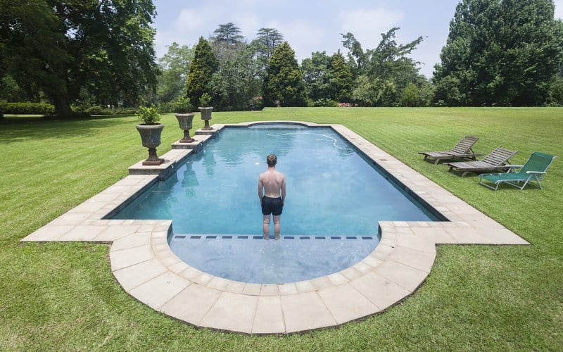 Young man standing on the edge of a tanning ledge of a roman style inground pool