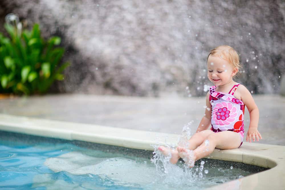 Little girl splashing her toes in the water of an inground pool