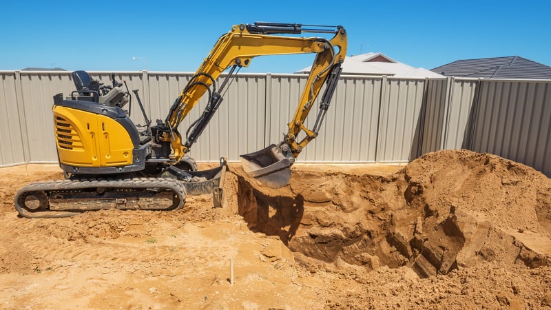 Small excavator in a backyard digging out a new pool