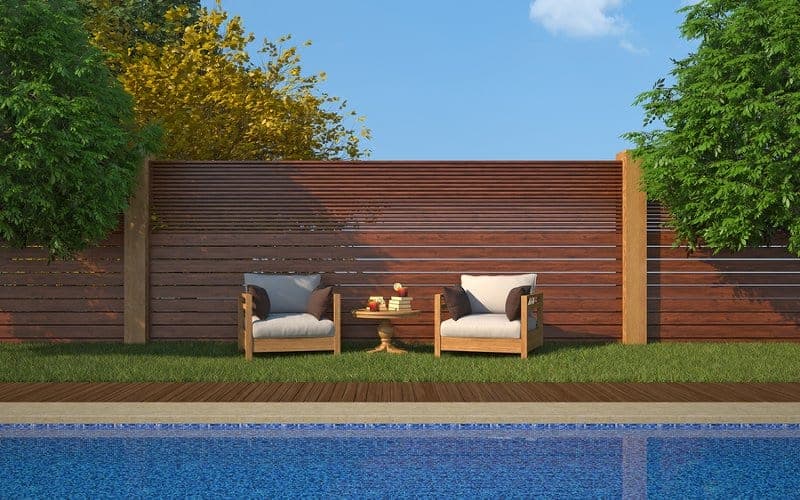 Two luxury outdoor chairs near an inground swimming pool with a high-end wooden pool fence in the background