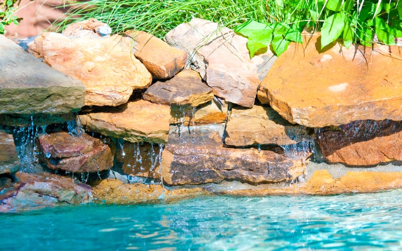 Rock waterfall pouring into an inground swimming pool