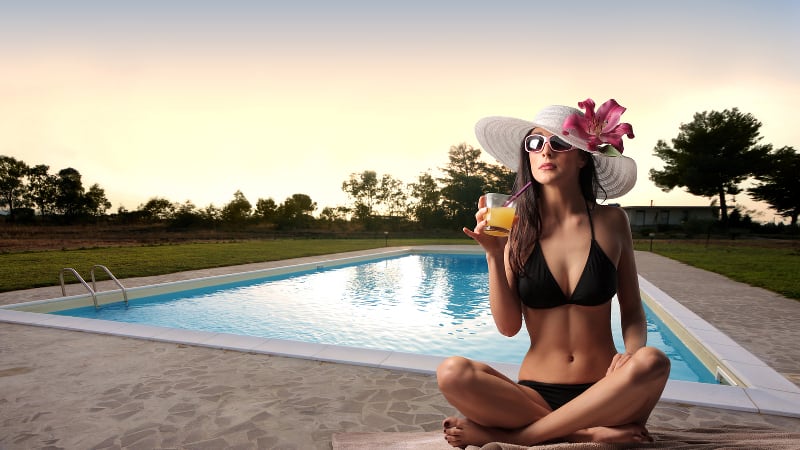 Glamorous young woman sitting by a swimming pool with a drink