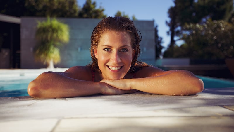 Woman leaning out of an inground swimming pool with a big smile on her face