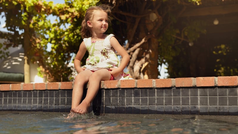 Little girl sitting on the edge of an inground swimming pool
