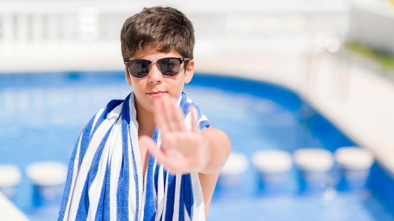 Boy holding up a hand as if to say stop in front of a swimming pool