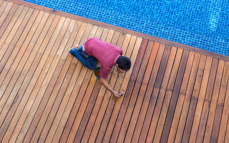 Worker staining beautiful wooden pool deck