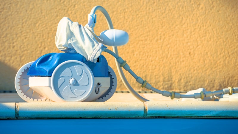 Robotic pool cleaner sitting at the edge of a pool