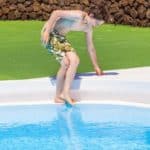 Boy dipping his toe in a swimming pool to test water temperature