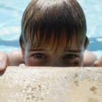 Boy peaking over the edge of a swimming pool