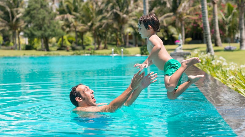 Child jumping into the arms of his father, who is waiting with outstretched arms in a swimming pool