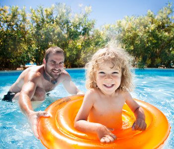 Father plays with his young son in a swimming pool.