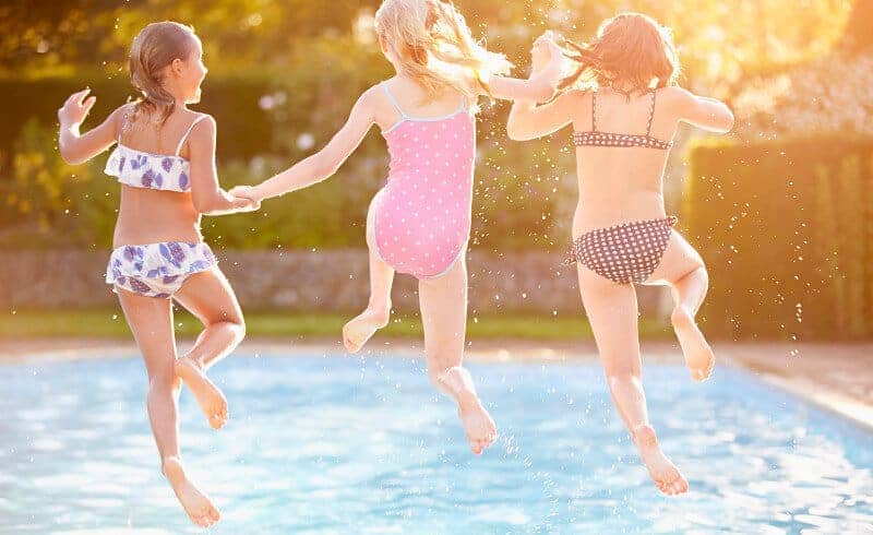 Three girls holding hands as they jump into a residential swimming pool