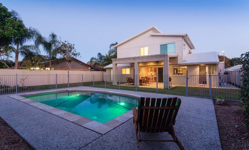 Small inground swimming pool and concrete deck with white house in the background