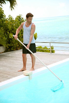 Man skimming a swimming pool with the beach in the background