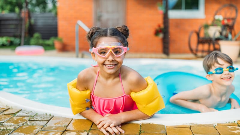 Two kids wearing safety floaties in an inground pool