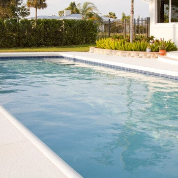 View of an inground swimming pool from the water, with an evergreen hedge maintaining privacy for swimmers