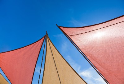 View of colorful shade sails from below, with a clear blue sky above.
