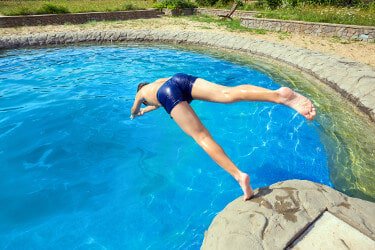 Teenage boy dives head first from a jump rock into a large naturalistic swimming pool