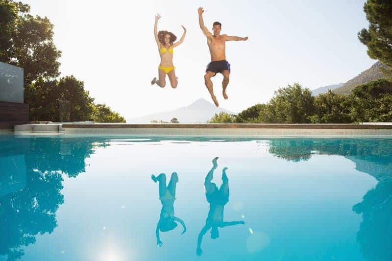 Couple jumping enthusiastically into clear swimming pool