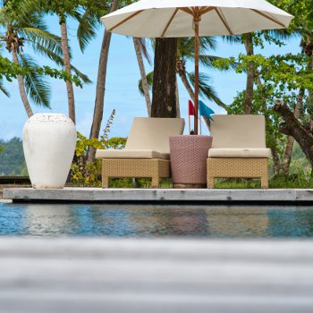 Two pool chairs sitting on a swimming pool deck next to a freestanding umbrella