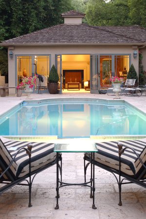 View of a lighted pool house next to an inground swimming pool, with two loungers in the foreground