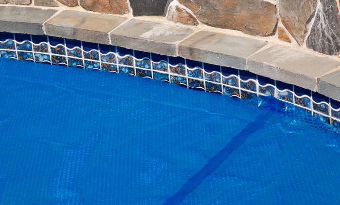 Closeup of the edge of an inground swimming pool covered with a blue bubble wrap solar pool cover