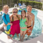 Family of four posing in the shallow water of an enclosed inground swimming pool