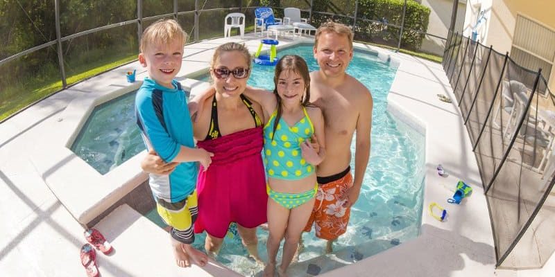 Family of four posing in the shallow water of an enclosed inground swimming pool