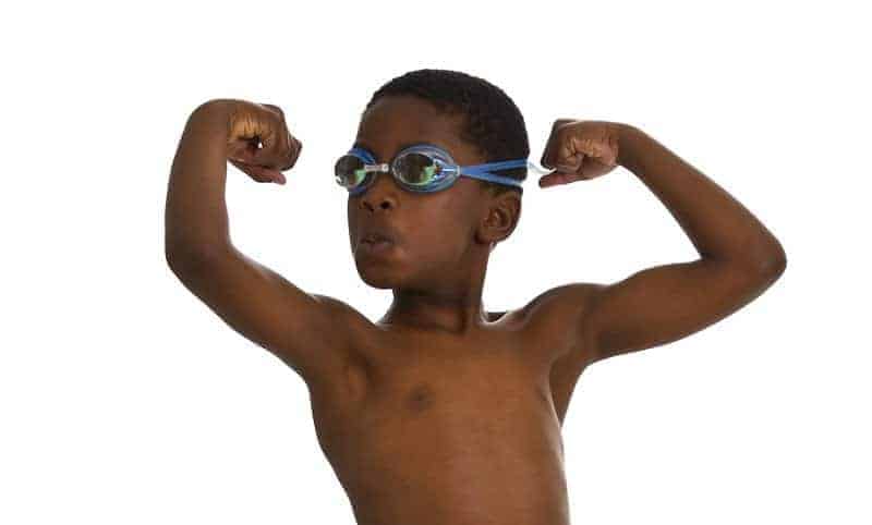 Young boy wearing swim trunks and goggles flexing his muscles