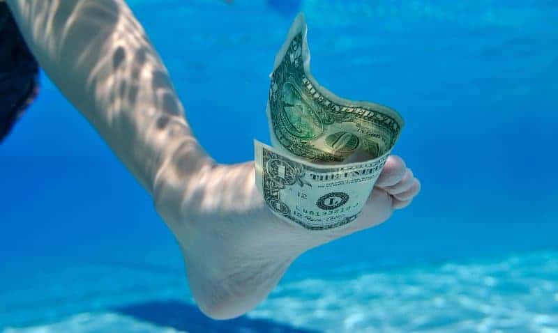 Underwater picture of a dollar bill held between the toes of a swimmer