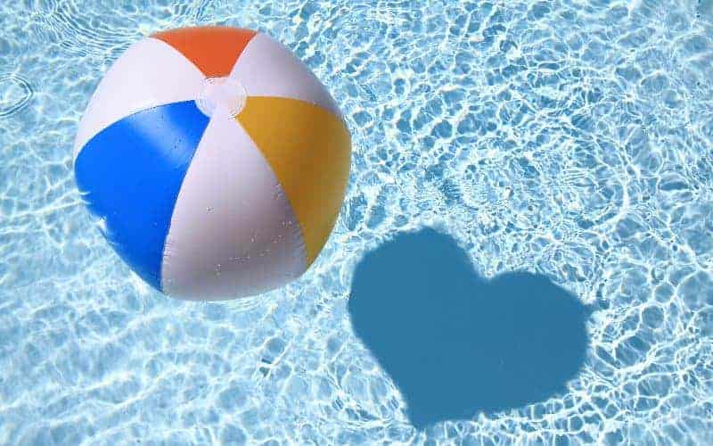 Beach ball floating on the surface of an inground swimming pool, casting a shadow in the shape of a heart
