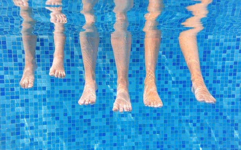 Underwater shot of the feet of three people dangling over the edge of an inground swimming pool in the water