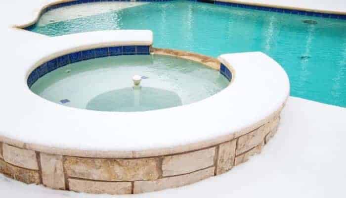 Picture of an inground swimming pool and spa during winter, with snow all around