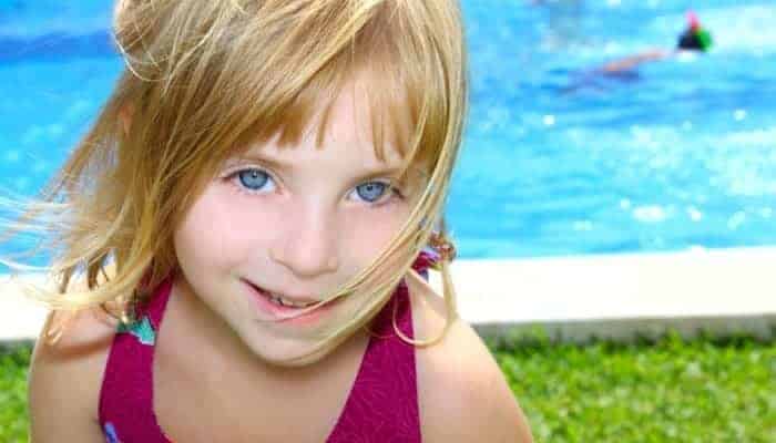 Young girl with grass-surround inground pool in the background