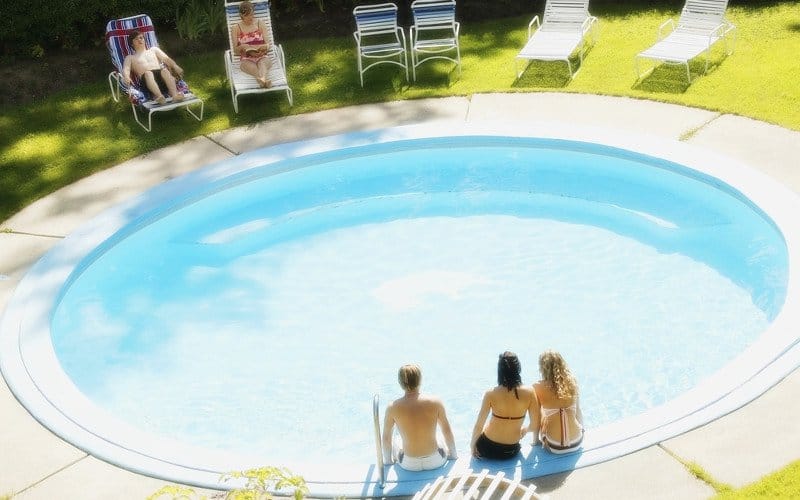 Group of people sitting around a round swimming pool on a summer day