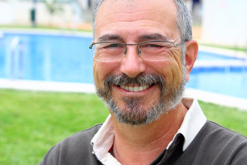 Retired man smiling in front of an inground swimming pool in his backyard