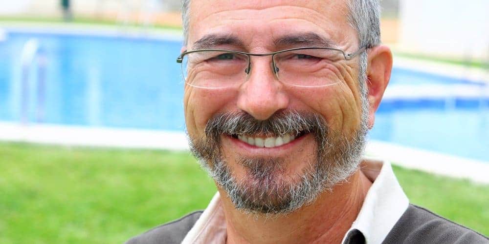 Retired man smiling in front of an inground swimming pool in his backyard