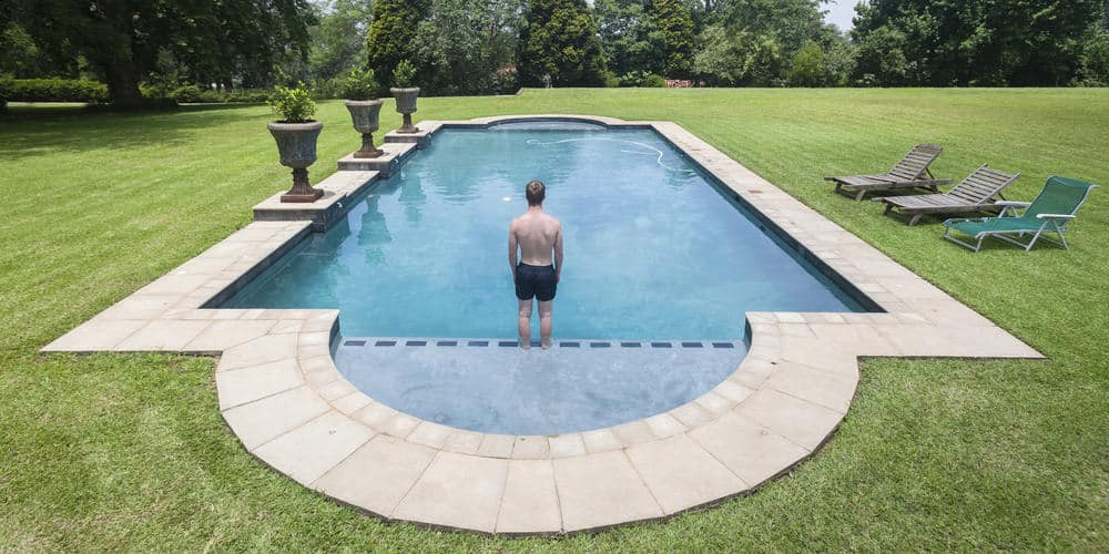 Young man standing on the edge of a tanning ledge of a roman style inground pool