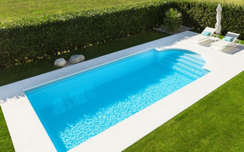Roman style pool with minimal white decking and a hedge for privacy