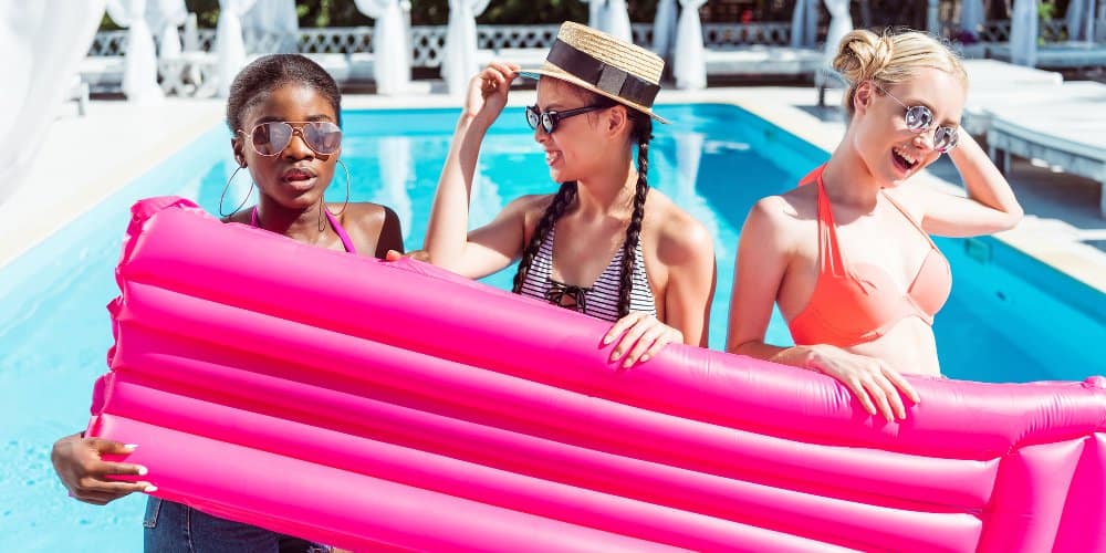 Three young ladies collectively holding an inflatable in front of a resort pool